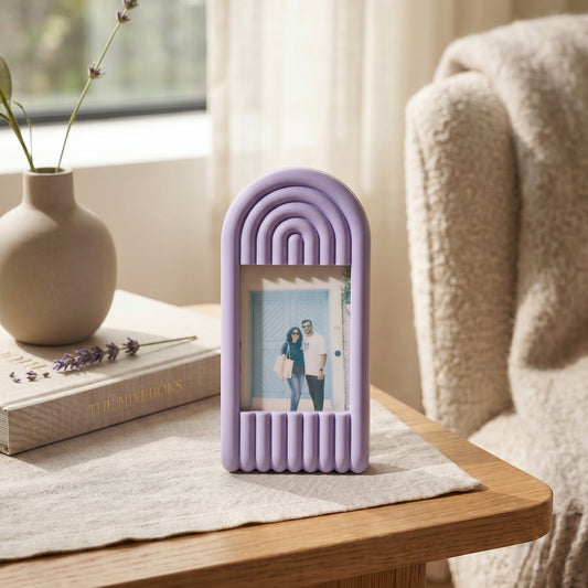 Purple decorative frame with a photo on a wooden table next to a vase and books.