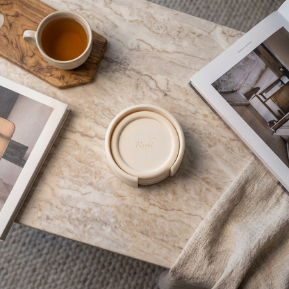 Round beige container with lid on a marble surface, next to a cup of tea and photo frames.