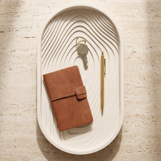 Brown leather notebook, keys, and pen on a decorative white tray with wavy design.