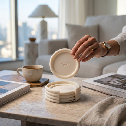 Person holding a set of coasters on a table with a cup and books in a bright room.