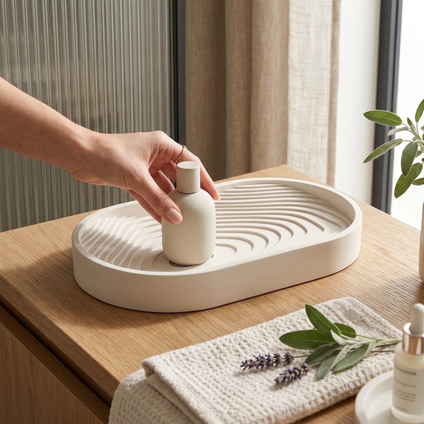 Hand placing a small white bottle on a textured tray with a plant and towel in the background