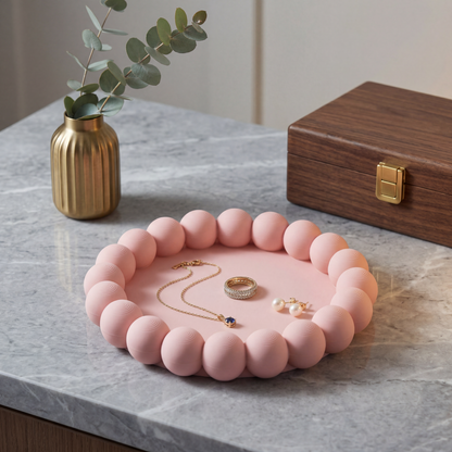 Pink jewelry tray with necklaces and rings on a marble surface, next to a gold vase and wooden box.