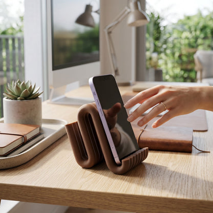 Person using a smartphone on a brown phone stand at a desk with a computer and decor.